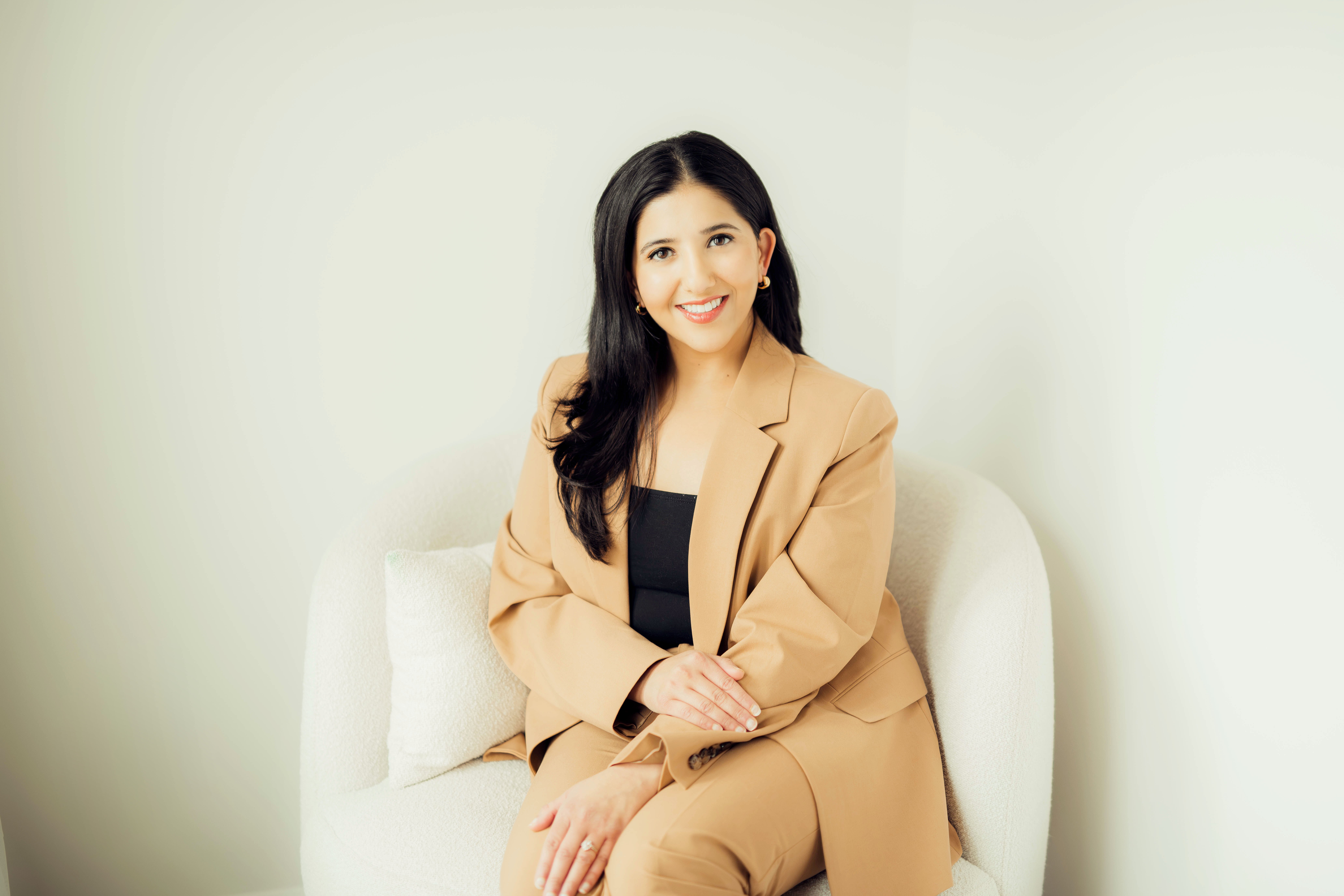 Dr. Zainab Aziz, board-certified endodontist, seated in a light-colored suit, smiling confidently, emphasizing patient-centered care and tooth preservation.