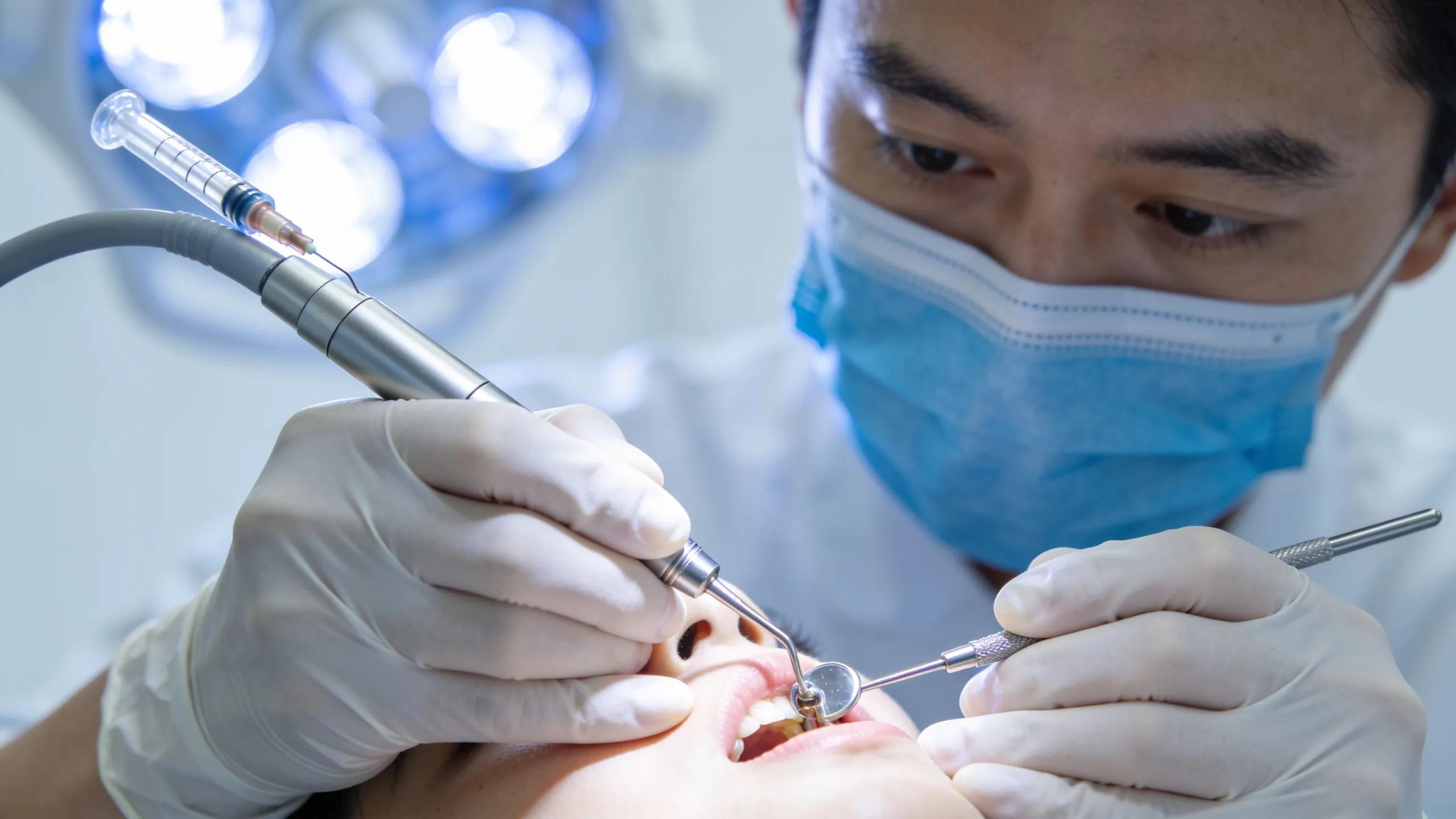 Dentist performing a root canal procedure with dental tools and bright lights highlighting the dental office